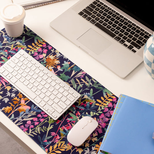 Laptop on a desk with a floral mouse pad, keyboard, and notebook.