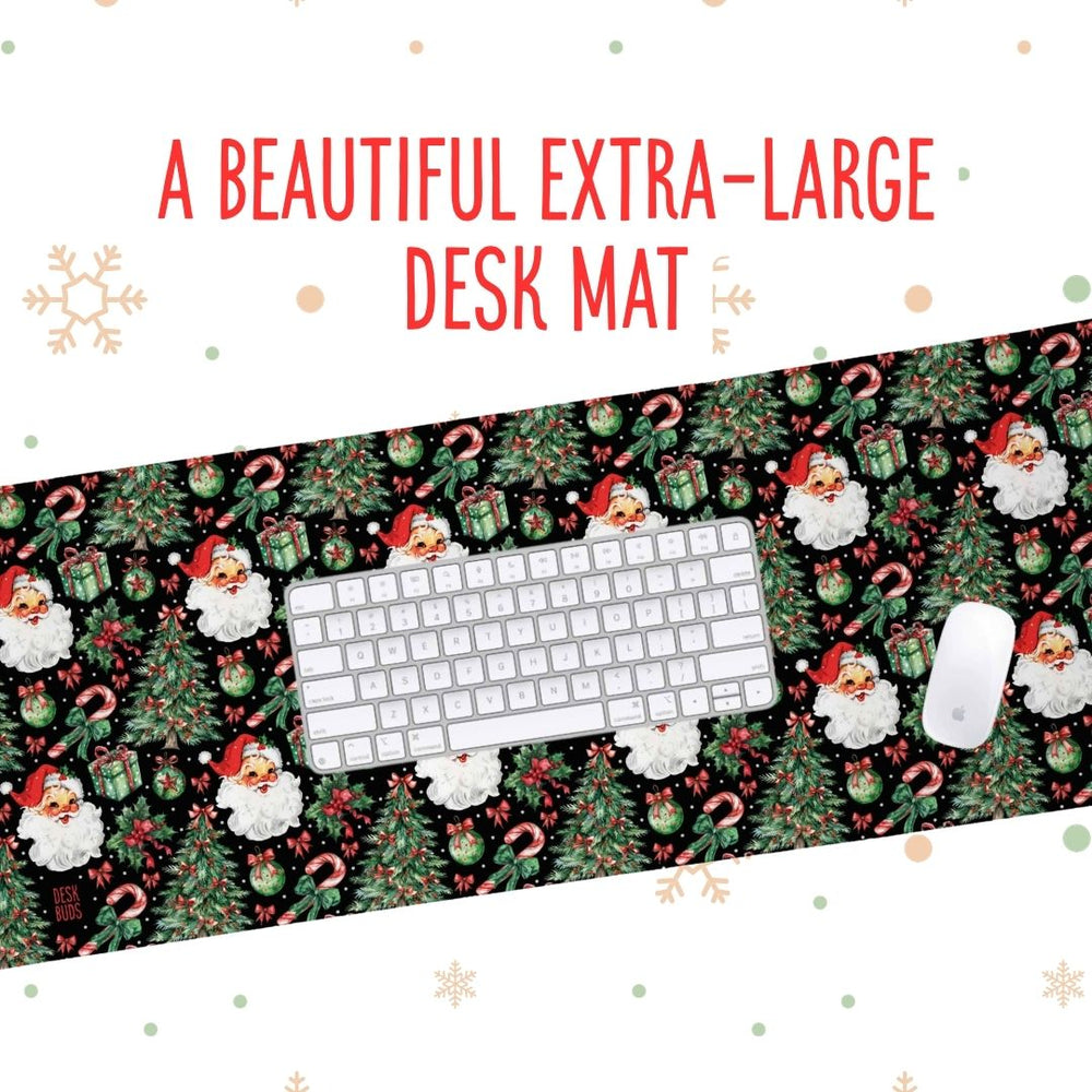 A Christmas-themed desk mat featuring a festive pattern of Santa Claus, snow globes, candy canes, and pine trees on a black background, shown with a white keyboard and mouse. Red text at the top reads 'A BEAUTIFUL EXTRA-LARGE DESK MAT'.
