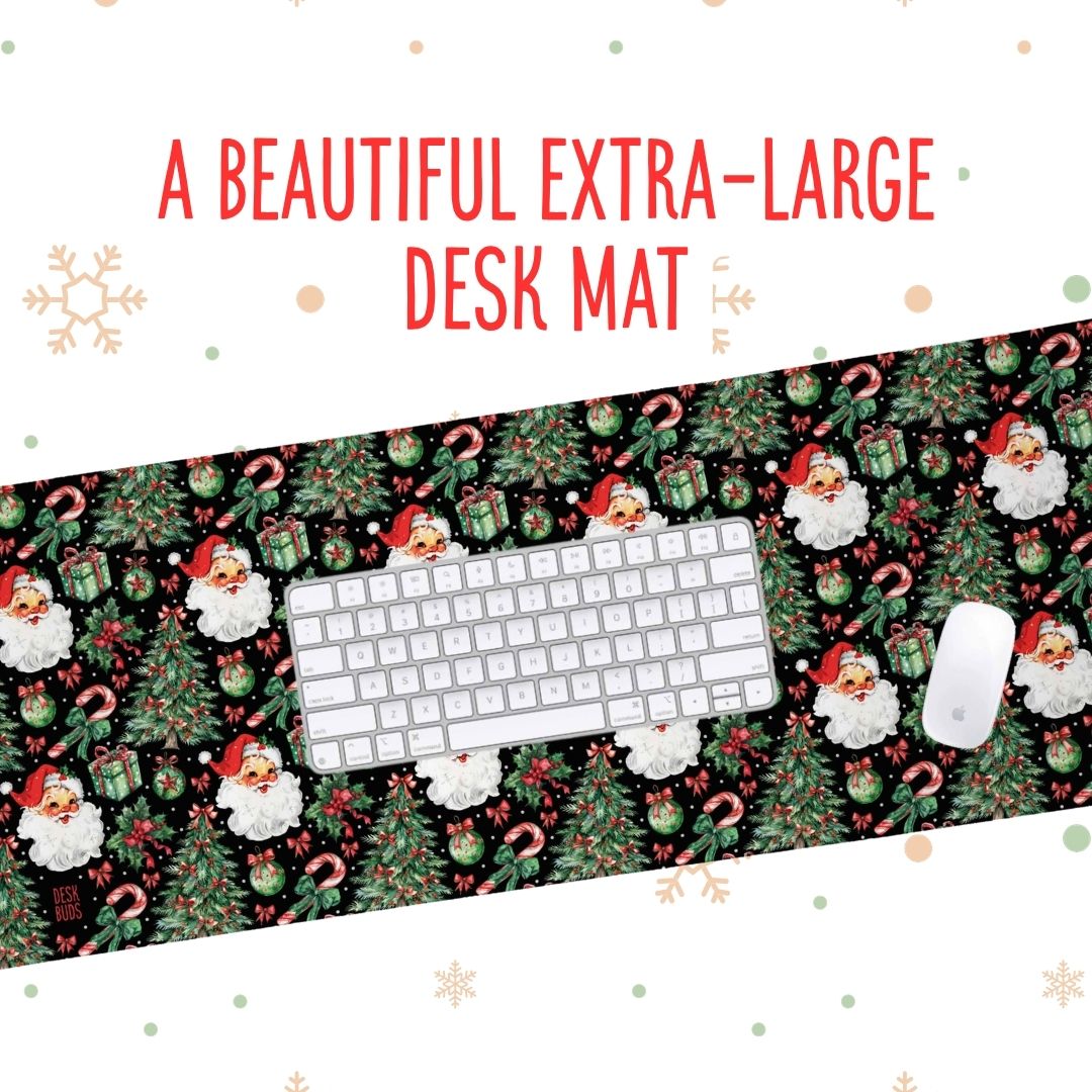 A Christmas-themed desk mat featuring a festive pattern of Santa Claus, snow globes, candy canes, and pine trees on a black background, shown with a white keyboard and mouse. Red text at the top reads 'A BEAUTIFUL EXTRA-LARGE DESK MAT'.